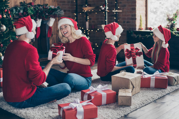 Full family dad mom two children exchanging x-mas gifts sitting cozy floor in decorated garland lights newyear room indoors wear santa caps red jumpers - Photo, Image