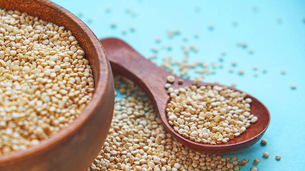 weiße Quinoa-Samen auf blauem Hintergrund. Quinoa in Schüssel und einem Löffel auf dem Küchentisch Ansicht. gesunde und ernährungsbewusste Superfood-Produkte. - Foto, Bild