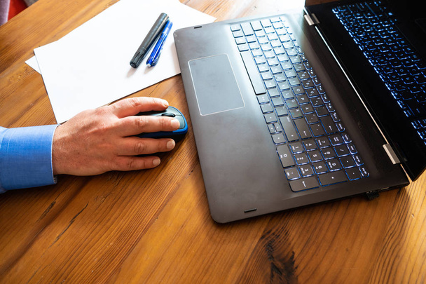 古い木製の机の上の黒いコンピュータ。青いシャツを着た男の手黒と青のペン白い紙の一部ビジネスとコミュニケーション。テキスト用のスペースを持つ背景写真. - 写真・画像
