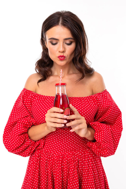 Γυναίκα με κόκκινο φόρεμα ποζάρουν με ποτό σε λευκό φόντο  - Φωτογραφία, εικόνα