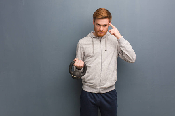 Young redhead fitness man thinking about an idea. Holding a dumbbell. - Фото, зображення