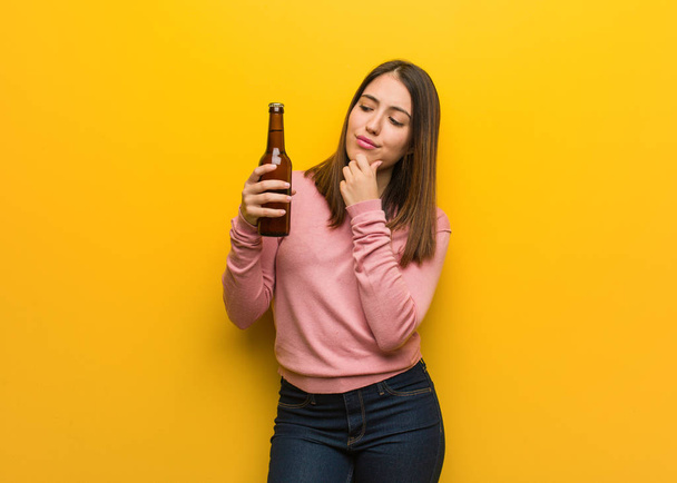 Jonge schattige vrouw met een biertje twijfelt en verward - Foto, afbeelding