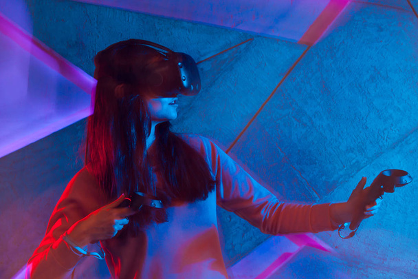 Une jeune femme en réalité virtuelle utilise des manettes, sur fond de mur décoré au néon
. - Photo, image