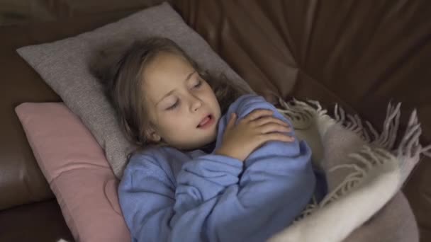 Young caucasian brunette girl in blue sweater laying under the warm blanket and coughing. Little child having fever and staying at home. - Video, Çekim
