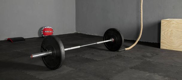 Barra de levantamientos con discos de varios pesos, pelota, caja,cuerda y cojin para ejercicios sobre piso de goma y pared gris - Photo, Image