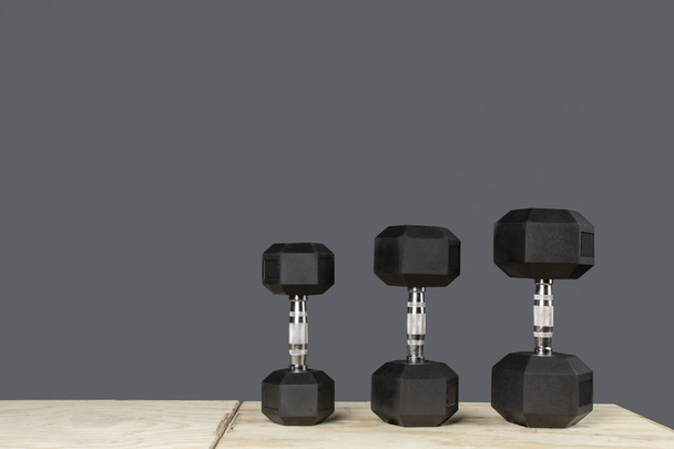 Dumbbells de varios pesos para ejercicios de crossfit sobre caja de madera y fondo gris - Foto, afbeelding