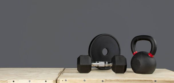 Hantel, Discos y Kettlebell de crossfit sobre caja de madera y fondo gris - Foto, Bild