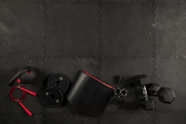 Dumbbell, cuerda, kettlebell, cojin y discotecas para hacer ejercicios de crossfit y fitness en piso de fondo color negro
 - Foto, Imagen