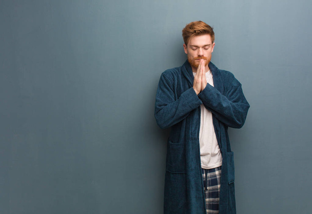 Young redhead man in pajama praying very happy and confident - Fotoğraf, Görsel