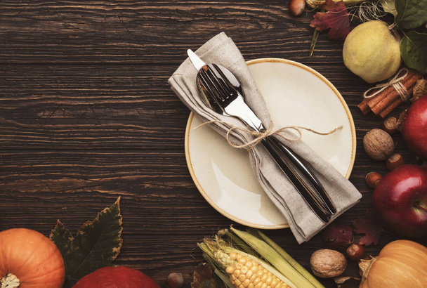 Thanksgiving dinner place setting. Autumn fruit, pumpkins, nuts, fallen leaves with plate and cutlery. Thanksgiving autumn background - Photo, Image