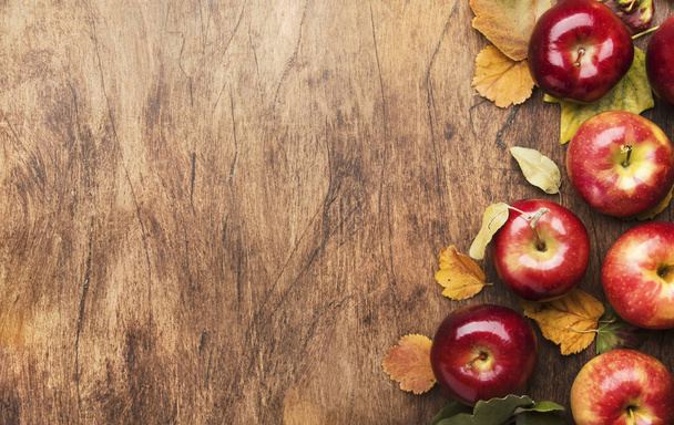 Autumn food background. Ripe apples with nuts, fallen leaves and cinnamon on rustic wooden table. Top view. Copy space - Фото, зображення