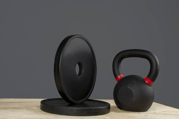 Discos de peso y kettlebell sobre caja de madera y fondo gris - Foto, Bild