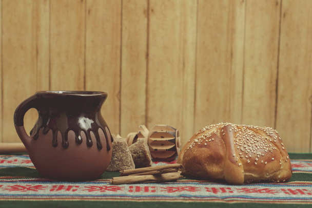 pan de muerto cortado con taza de cafe, canela y piloncillo en fondo de madera - Foto, Bild