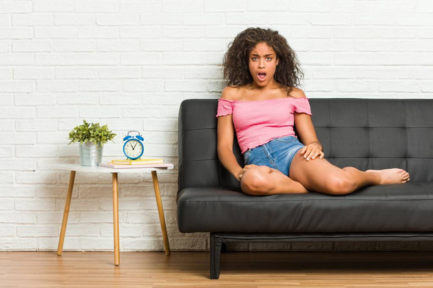 Młody African American kobieta siedzi na kanapie krzyczeć bardzo zły i agresywny. - Zdjęcie, obraz