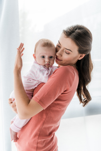 attractive mother holding in arms baby daughter at home  - Foto, imagen
