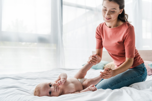 happy mother touching legs of baby lying on bed  - Zdjęcie, obraz