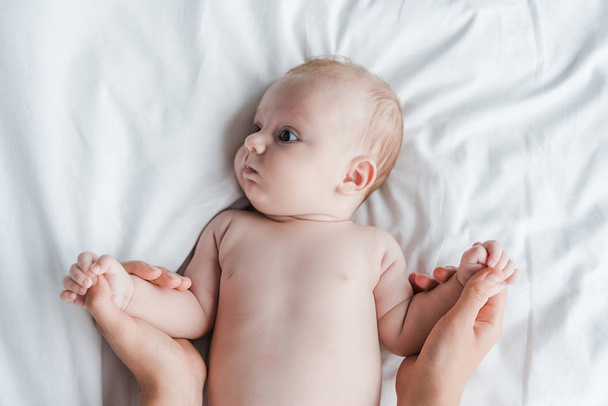 felső nézet anya kézen fogva csecsemő lánya feküdt az ágyban  - Fotó, kép