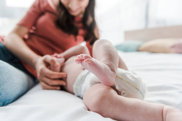selective focus of barefoot of cute infant near mother on bed  - Φωτογραφία, εικόνα