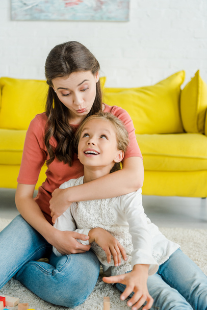 attractive babysitter looking at happy kid in living room  - Foto, Imagen