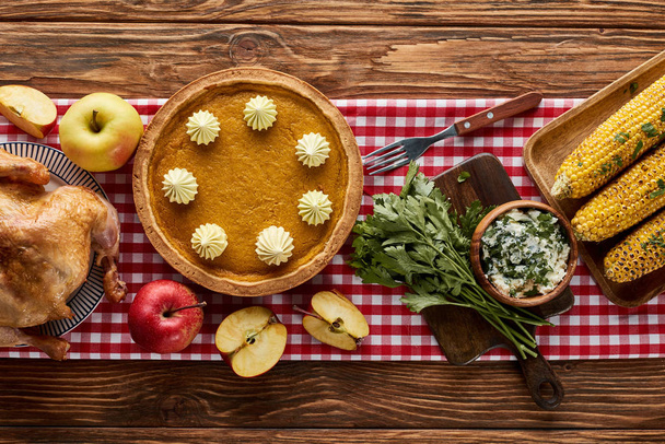 vue du dessus de la dinde rôtie, tarte à la citrouille et serviette à carreaux rouge de maïs grillé sur table en bois
 - Photo, image