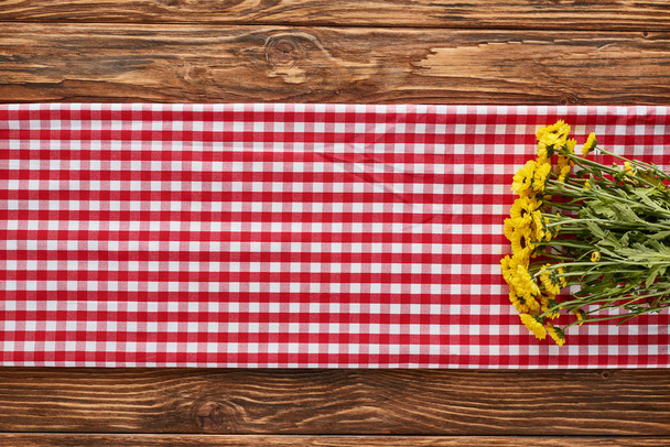top view of yellow wildflowers on plaid red napkin on wooden table - Φωτογραφία, εικόνα