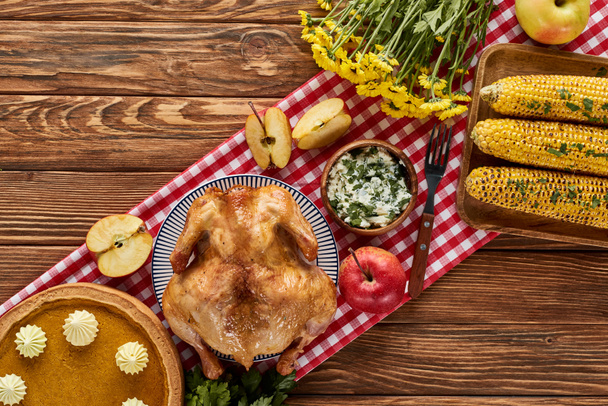 felülnézet pörkölt pulyka, sütőtök pite és grillezett zöldségek felszolgált fa asztalon virágok és kockás szalvéta - Fotó, kép
