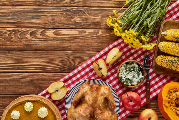 top view of roasted turkey, pumpkin pie and grilled vegetables served on wooden table with flowers and plaid napkin - Foto, Bild