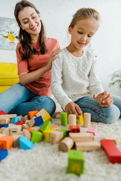 selective focus of kid playing with toy blocks near cheerful babysitter - Φωτογραφία, εικόνα