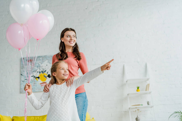 happy kid pointing with finger while holding pink balloons near babysitter - Foto, Imagen