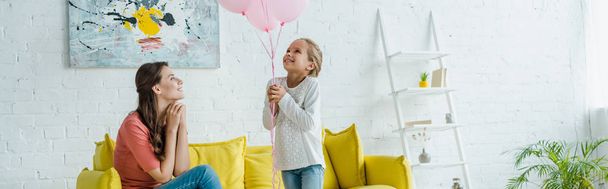 panoramic shot of cheerful babysitter looking at pink balloons near happy kid  - Fotó, kép