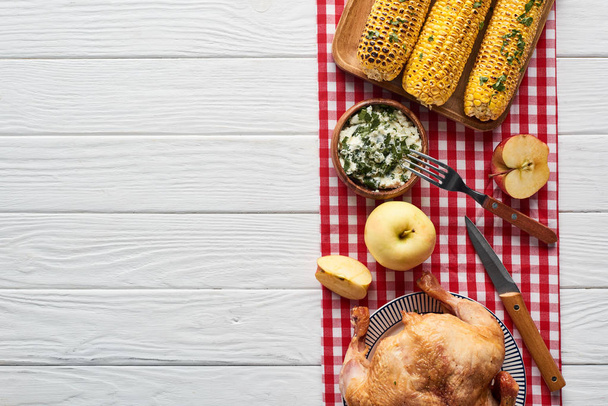 top view of roasted turkey, apples and grilled corn served on white wooden table with red plaid napkin - Photo, Image