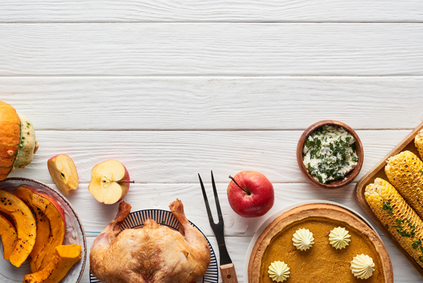ローストターキー、カボチャのパイと赤の再生ナプキンと白い木製のテーブルで提供されるグリルコーンのトップビュー - 写真・画像
