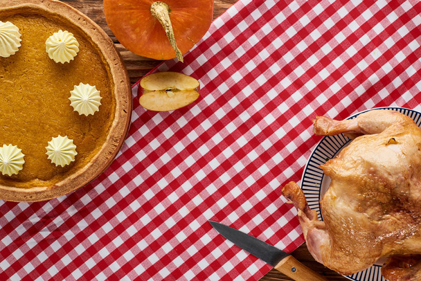 top view of roasted turkey, pumpkin pie and pumpkin served on plaid red napkin on wooden table - Fotografie, Obrázek