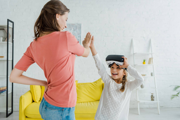 cheerful kid in virtual reality headset giving high five to babysitter at home  - Фото, зображення
