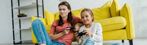 KYIV, UKRAINE - SEPTEMBER 4, 2019: panoramic shot of emotional babysitter and happy kid playing video game in living room  - Photo, image