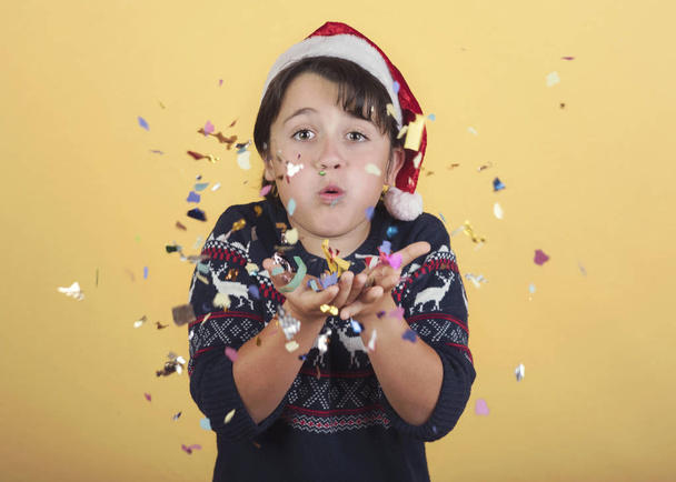 criança soprando confete vestindo Natal Papai Noel Chapéu
 - Foto, Imagem