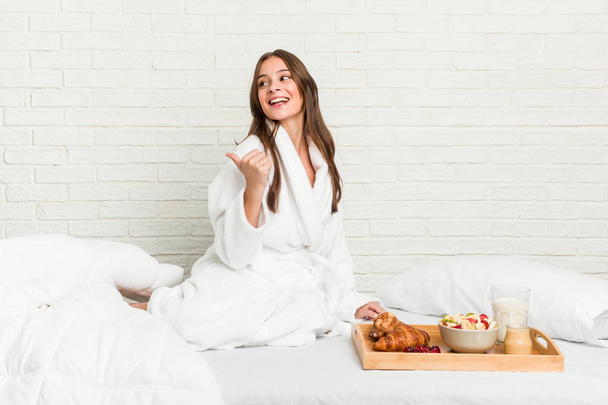 Giovane donna caucasica sui punti del letto con il pollice lontano, ridendo e spensierato
. - Foto, immagini