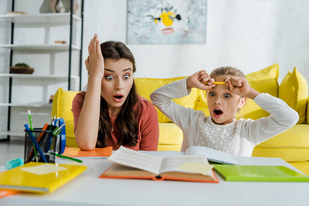 Selektiver Fokus eines geschockten Kindes beim Anblick eines Buches in der Nähe eines überraschten Babysitters im Wohnzimmer  - Foto, Bild