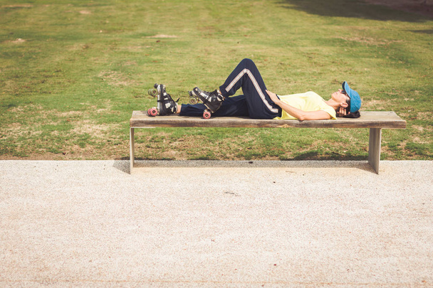 Vrouw met rolschaatsen rust ontspannen op een park bank - Foto, afbeelding