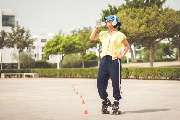 Vrouw met rolschaatsen neemt een pauze om water te drinken - Foto, afbeelding