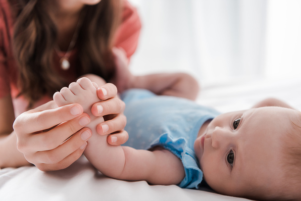 cropped view of mother holding hand of cute baby daughter in bedroom  - Foto, afbeelding
