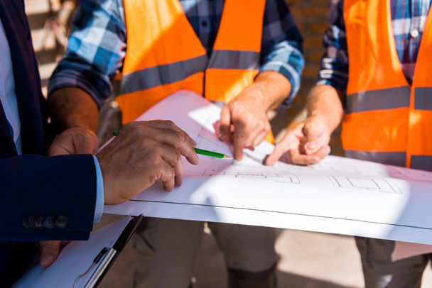 cropped view of businessman holding pencil near blueprint and builders  - Photo, Image