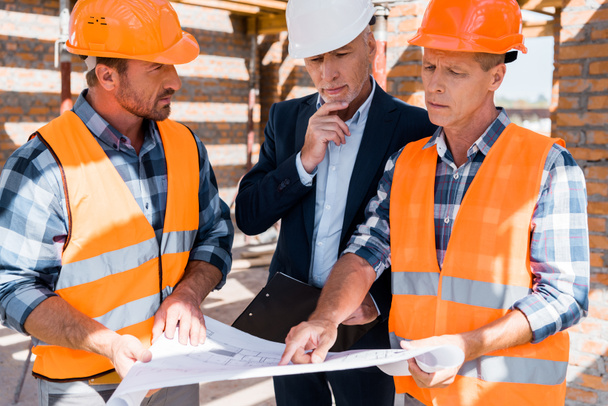 mature constructor pointing with finger at blueprint near businessman  - Foto, afbeelding