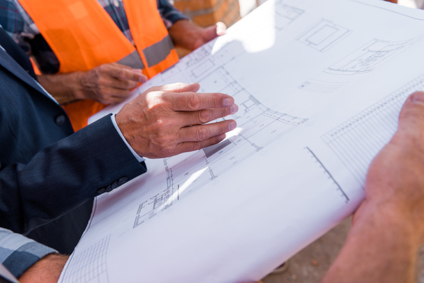 cropped view of businessman gesturing near blueprint and constructors  - Photo, Image