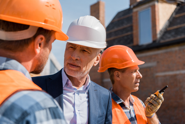 selective focus of constructor near bearded businessman and coworker in helmets  - Φωτογραφία, εικόνα