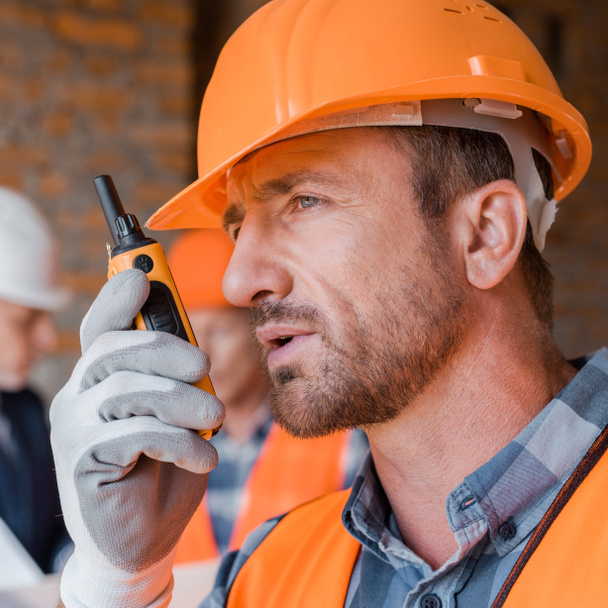 selective focus of handsome builder talking while holding walkie talkie  - Photo, image