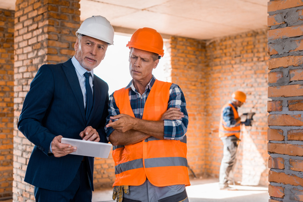 selective focus of businessman standing near builder pointing with finger at digital tablet  - Photo, Image