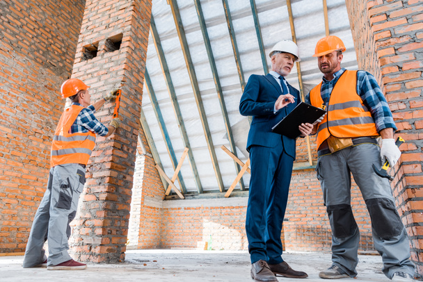 mature bearded businessman holding clipboard near builders - Fotografie, Obrázek