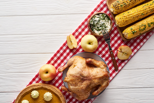 сверху вид тыквенного пирога, индейки и овощей подается за белым деревянным столом на красной клетчатой салфетке на ужин в День Благодарения
 - Фото, изображение