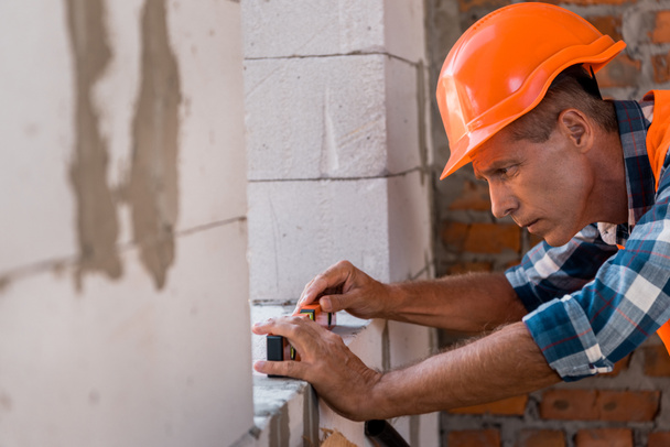 selective focus of middle aged constructor in helmet measuring concrete wall  - 写真・画像